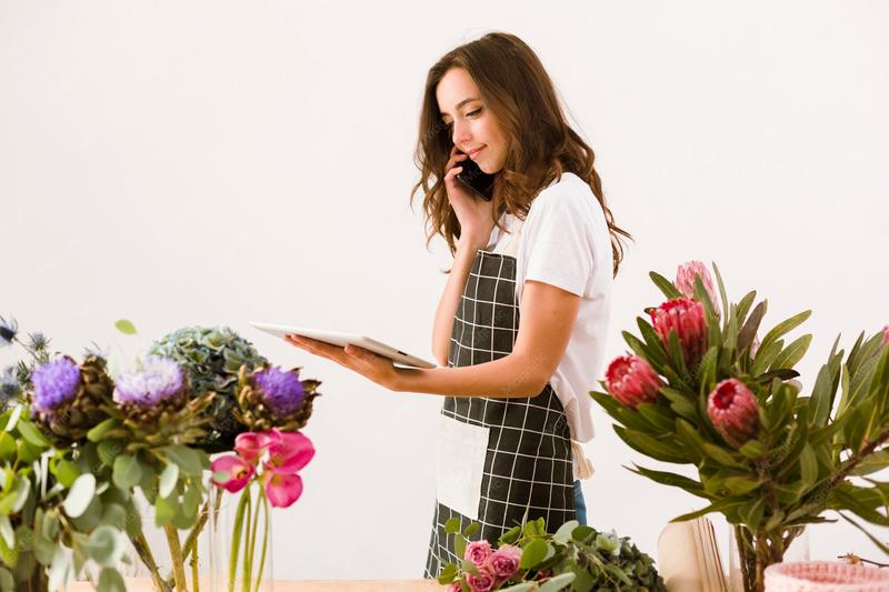 A florist with a phone and a tablet among the stock